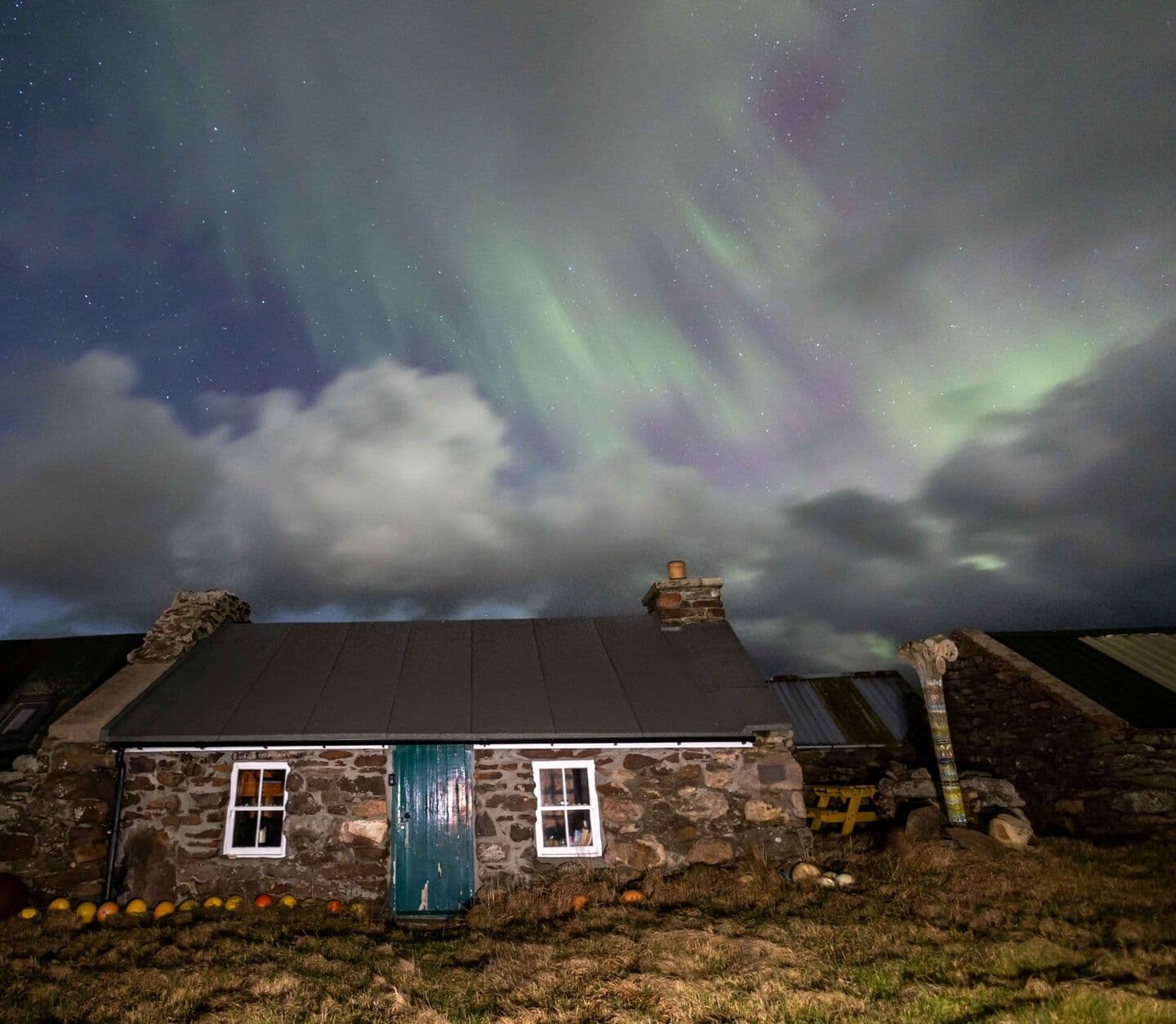Green curtains of the Northern Lights over the front of the böd, its green door and lit windows