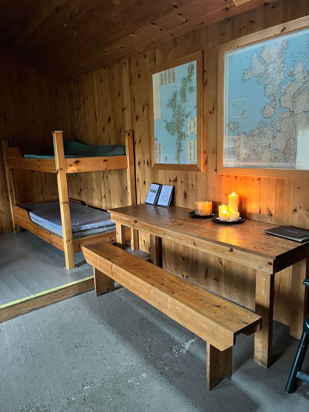 Wooden bunk beds with mattresses beside a table and bench, maps of Shetland on the pine-panelled wall